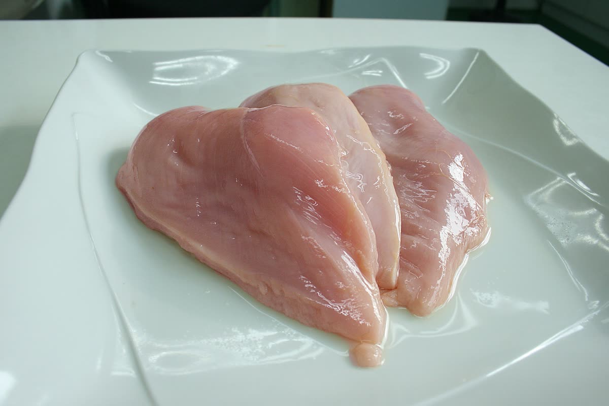 Three raw skinless chicken breasts overlapping in the centre of a white plate
