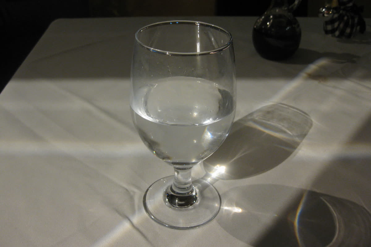 A glass of water on a white linen tablecloth with sunlight refracting through it